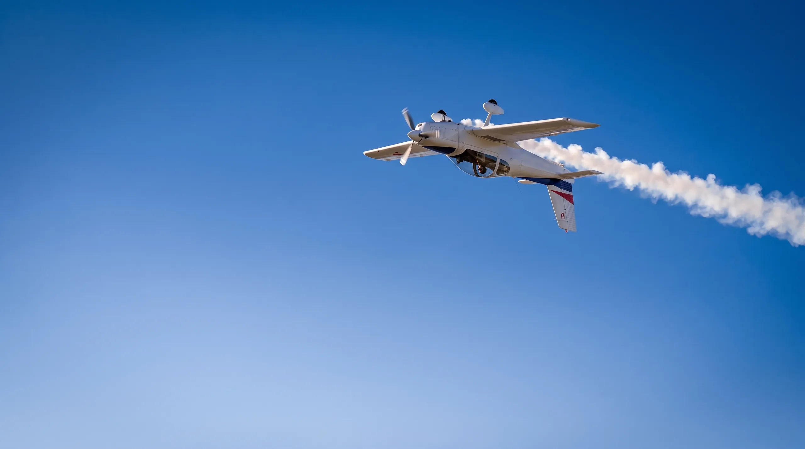 Aerobatic aircraft flying inverted with a smoke trail against a blue sky